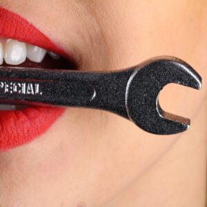 woman holding wrench in mouth with her straight teeth, signifying dental work or OMT