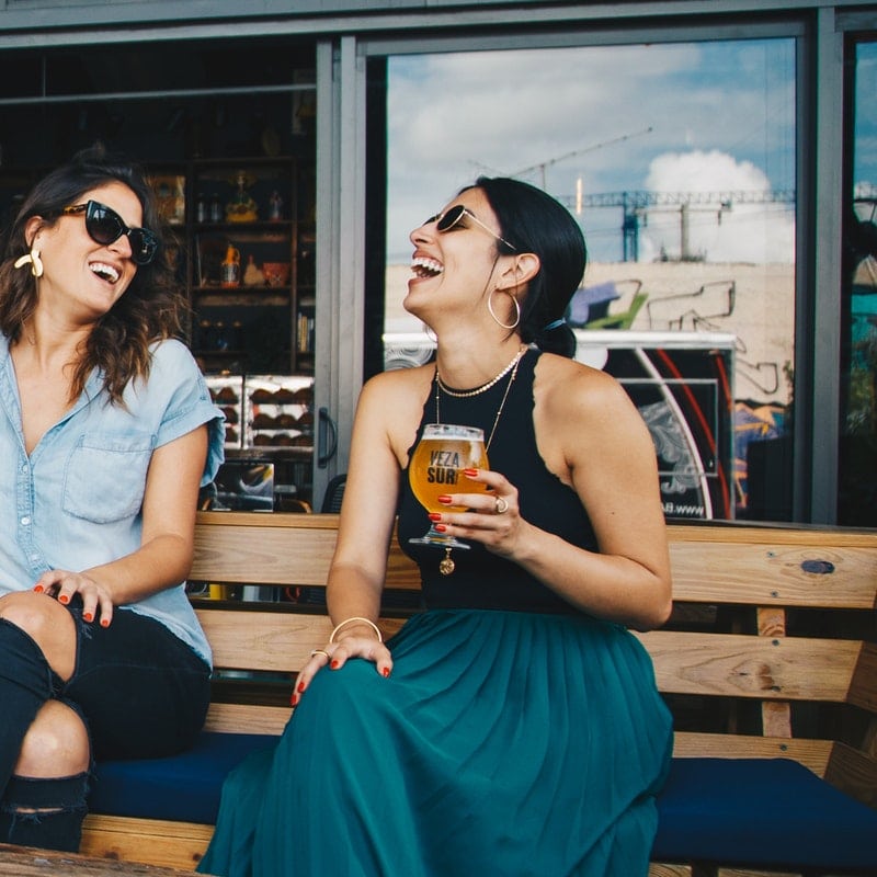 two girls laughing over drinks at an outdoor patio